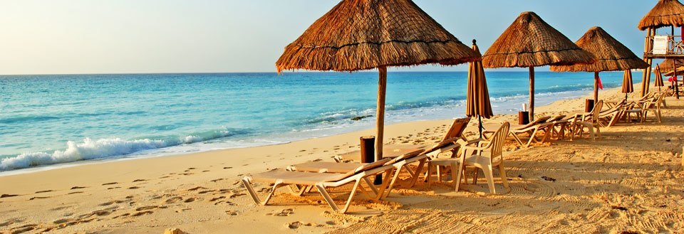En solig strand med stråparasoller och solstolar vända mot det lugna turkosblå havet.