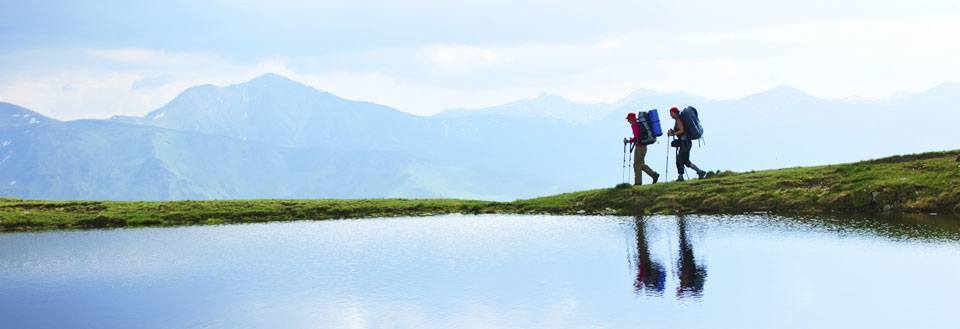 Två vandrare med ryggsäckar vandrar vid en bergstjärn med en magnifik utsikt över bergen.