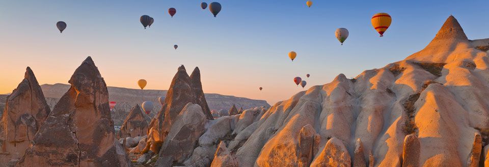 Färgglada varmluftsballonger som svävar över ett unikt klippformat landskap i solnedgången.