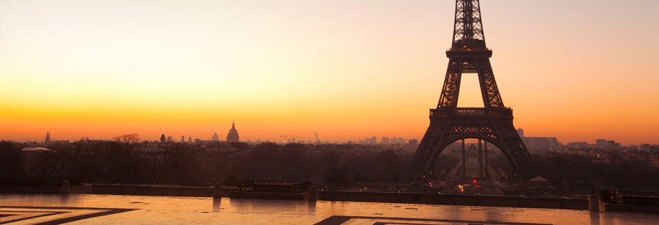 Solnedgången bakom Eiffeltornet i Paris med en varm orange himmel och stadens siluett synlig.