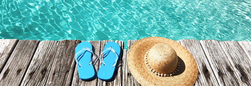 Blåa flip-flops och en stråhatt ligger på en träbrygga bredvid en pool.