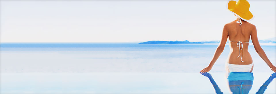 Bild av en pittoresk by med vita hus, röda tak och grönskande växter under en klarblå himmel.