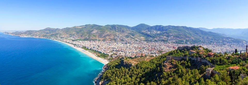 Panoramavy över Antalya med blått vatten, stränder och gröntäckta berg i bakgrunden.