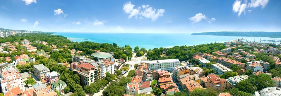 Panoramavy över Varna med tätt liggande bostäder, omgiven av träd och med ett azurblått hav i bakgrunden. Panoramavy över Varna med tätt liggande bostäder, omgiven av träd och med ett azurblått hav i bakgrunden.