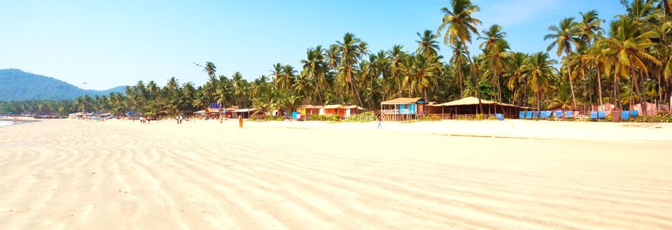 Solig strand med palmer och färgglada stugor längs kustlinjen.