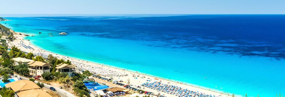 Panoramavy över en livlig strand med parasoll och klarblått hav.
