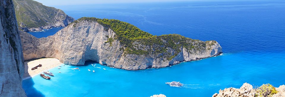 Panorama av en idyllisk vik med turkosblått vatten, omgivet av klippor och en strand.
