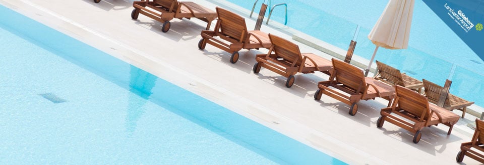 Solstolar och en vit parasoll placerade vid kanten av en inbjudande swimmingpool. Solstolar och en vit parasoll placerade vid kanten av en inbjudande swimmingpool.
