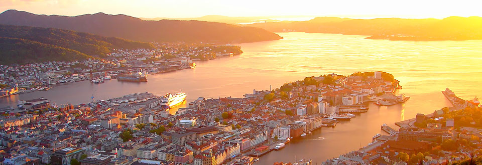 Bild av en stad vid solnedgången med berg i bakgrunden och en skimrande flod eller fjord framtill.