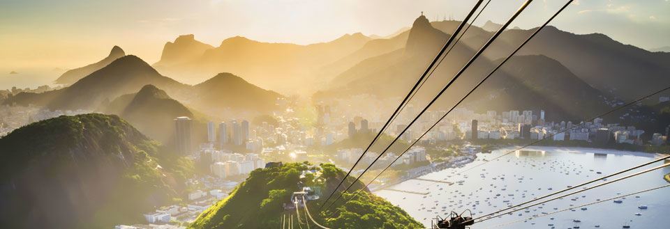 Bild av en linbana med utsikt över Rio de Janeiro omgiven av kullar och vatten vid solnedgång.