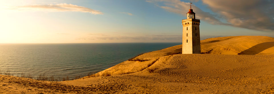 Rubjerg Knude  vid kusten, omgiven av sanddyner under en gyllene solnedgång.