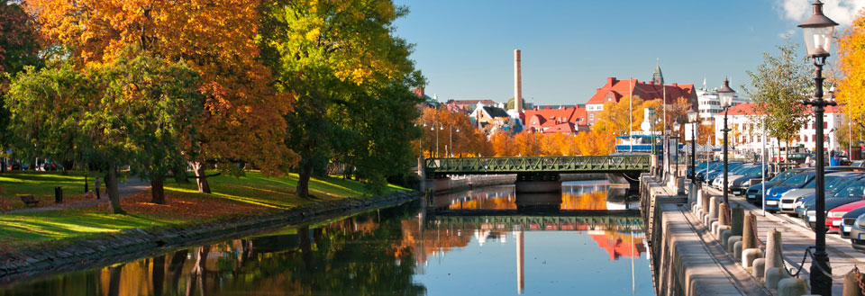 Fridfull flod genom en stad med färggranna höstträd och en klarblå himmel.