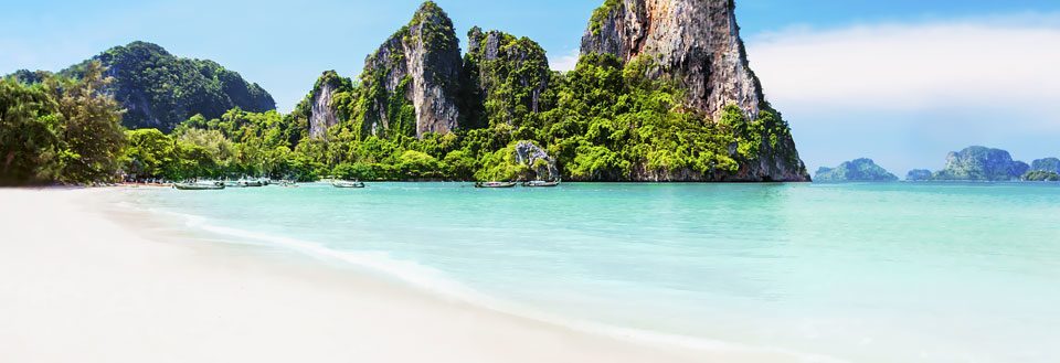 Tropisk paradis med vit sandstrand, turkos vatten och lummiga gröna klippöar.