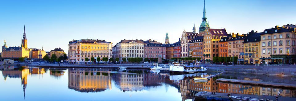 En pittoresk utsikt över Stockholm vid vattnet på morgonen. Byggnadernas spegling syns i det lugna vattnet.