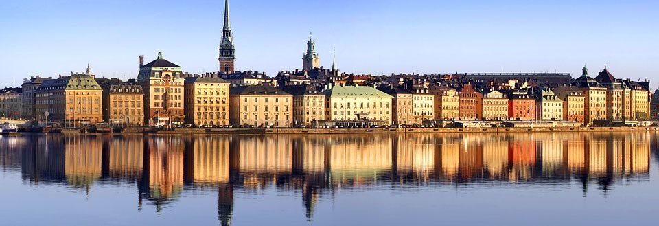 Panoramavy över Stockholms byggnader speglade i vattnet vid solnedgången.