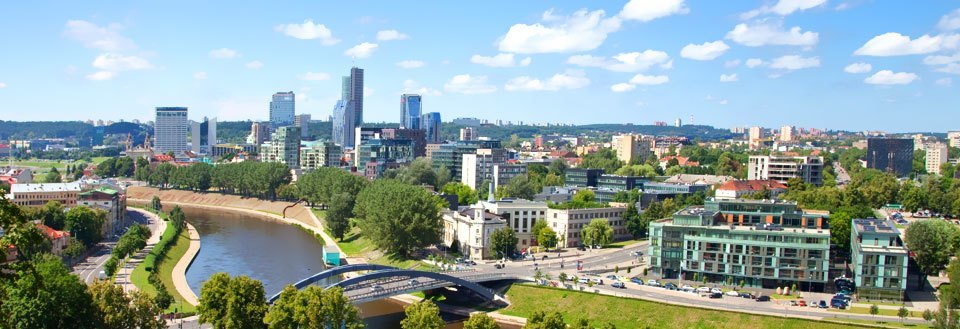 Panoramavy över Vilnius med moderna byggnader, en flod och en bro under en klarblå himmel.