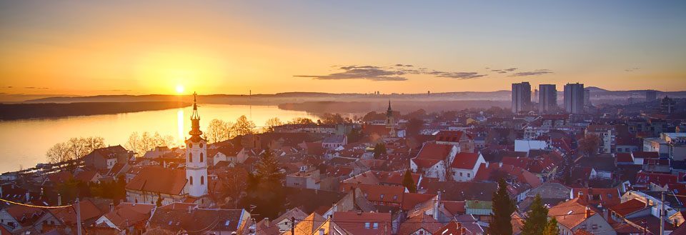 Stad vid solnedgången med silhuetten av en kyrka och moderna byggnader i bakgrunden.