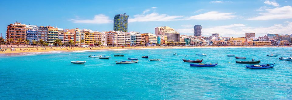 Strålande vid Gran Canarias strandkant med mångfärgade hus och småbåtar i det kristallklara vattnet.