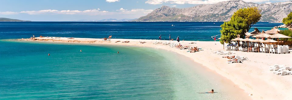 Inbjudande strand med kristallklart vatten, sandstrand och berg i bakgrunden.