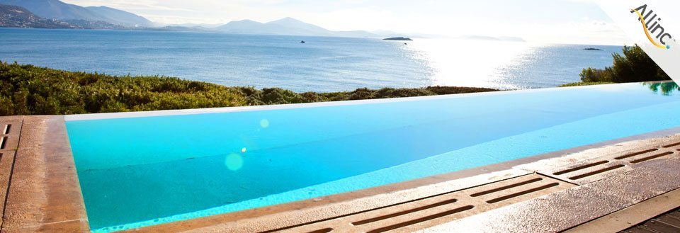 En lockande infinity-pool med utsikt över en solig kust och berg i fjärran.